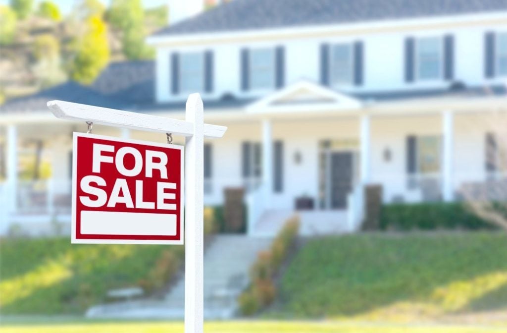 A for sale sign is shown in front of a beautiful starter home, it is blurred in the background. 