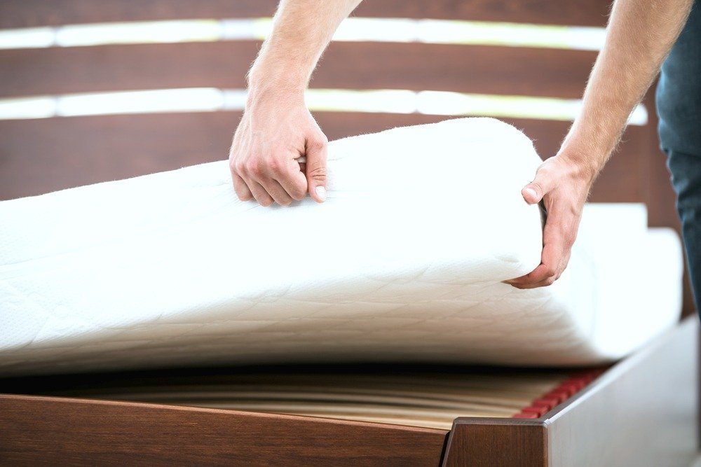 A man lifts a mattress from the frame. 