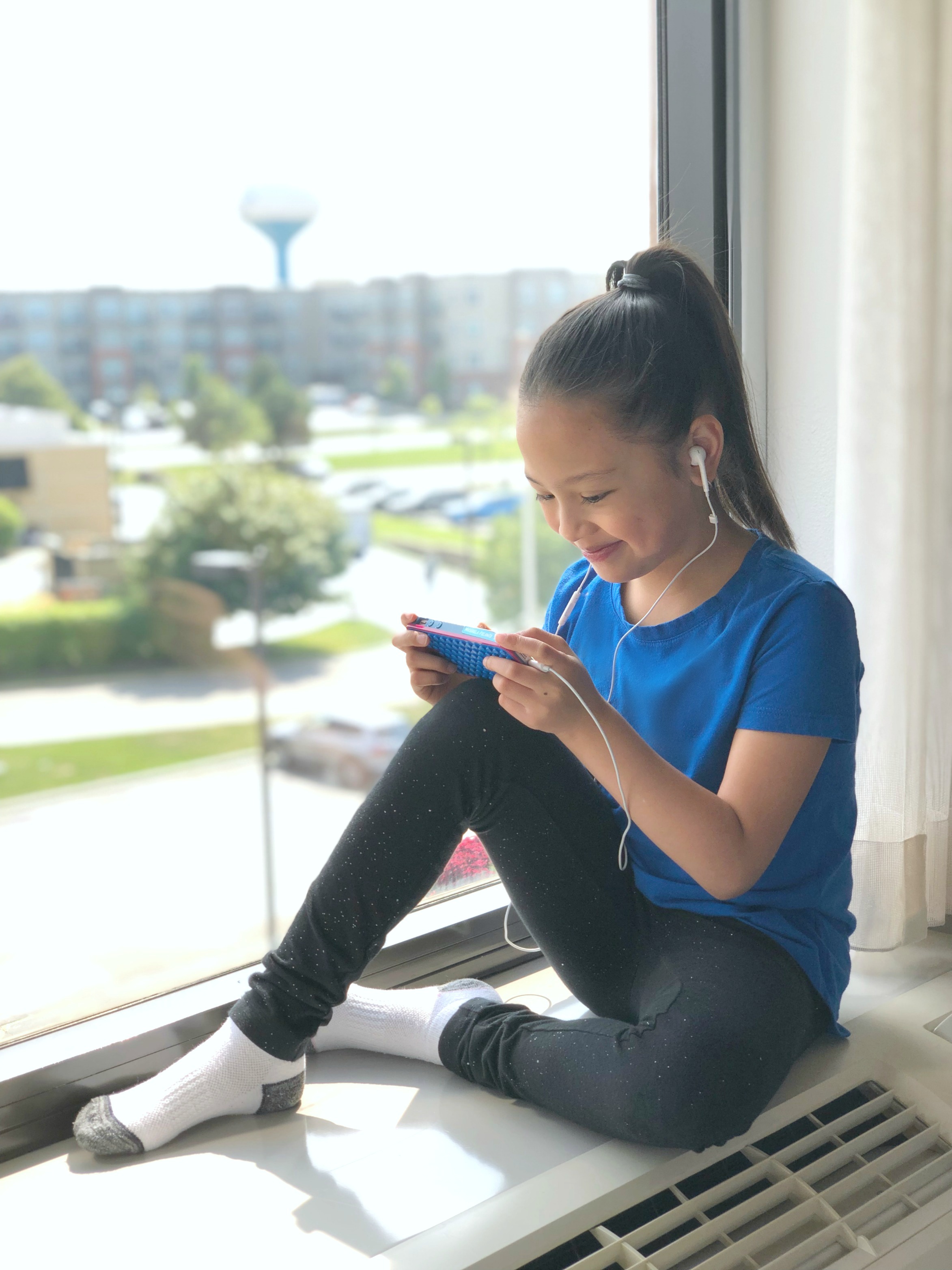 Mimi sits on a ledge at a hotel and watches YouTube.