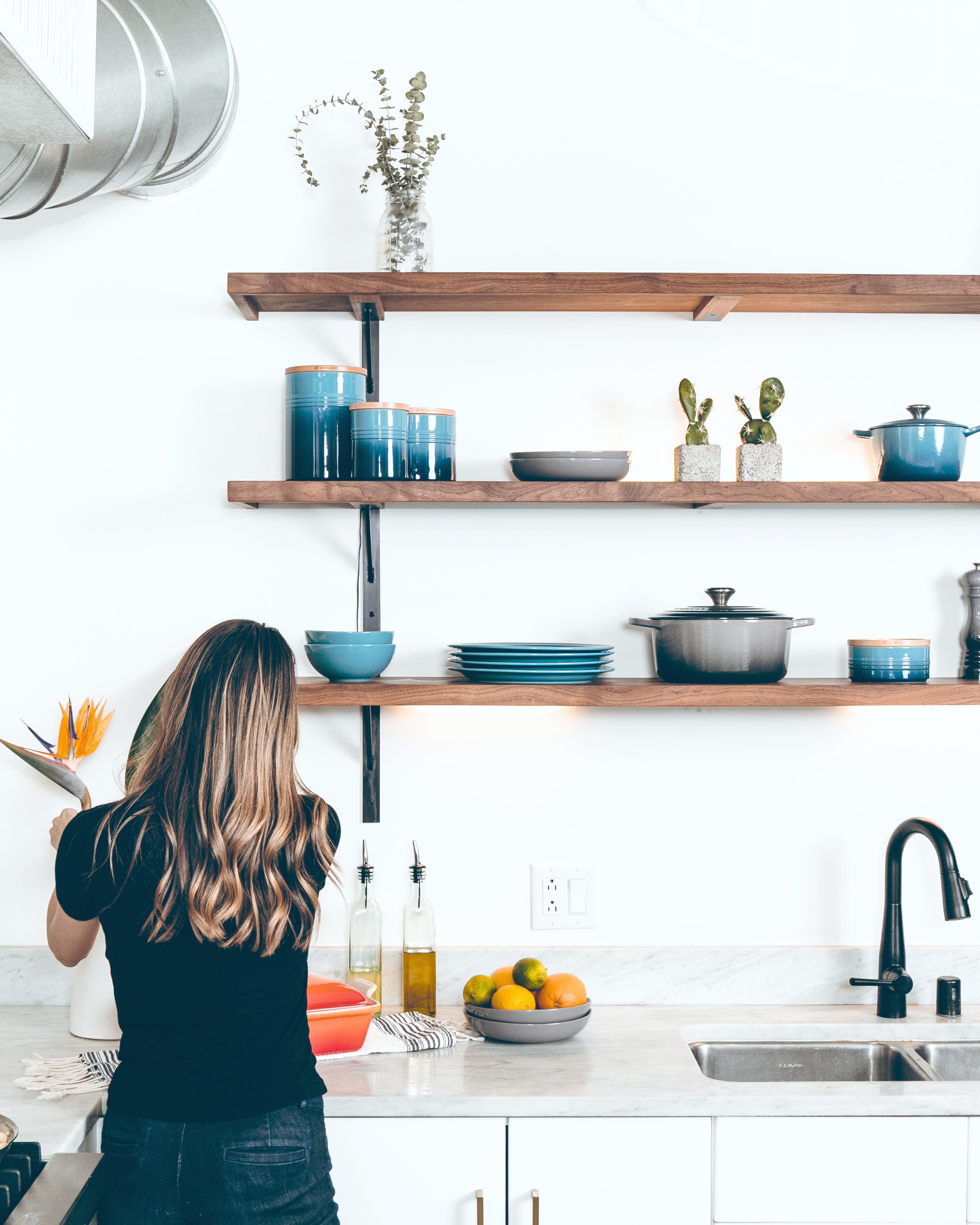 A woman adds flowers to her beautiful modern kitchen. The kitchen has exposed shelves. 