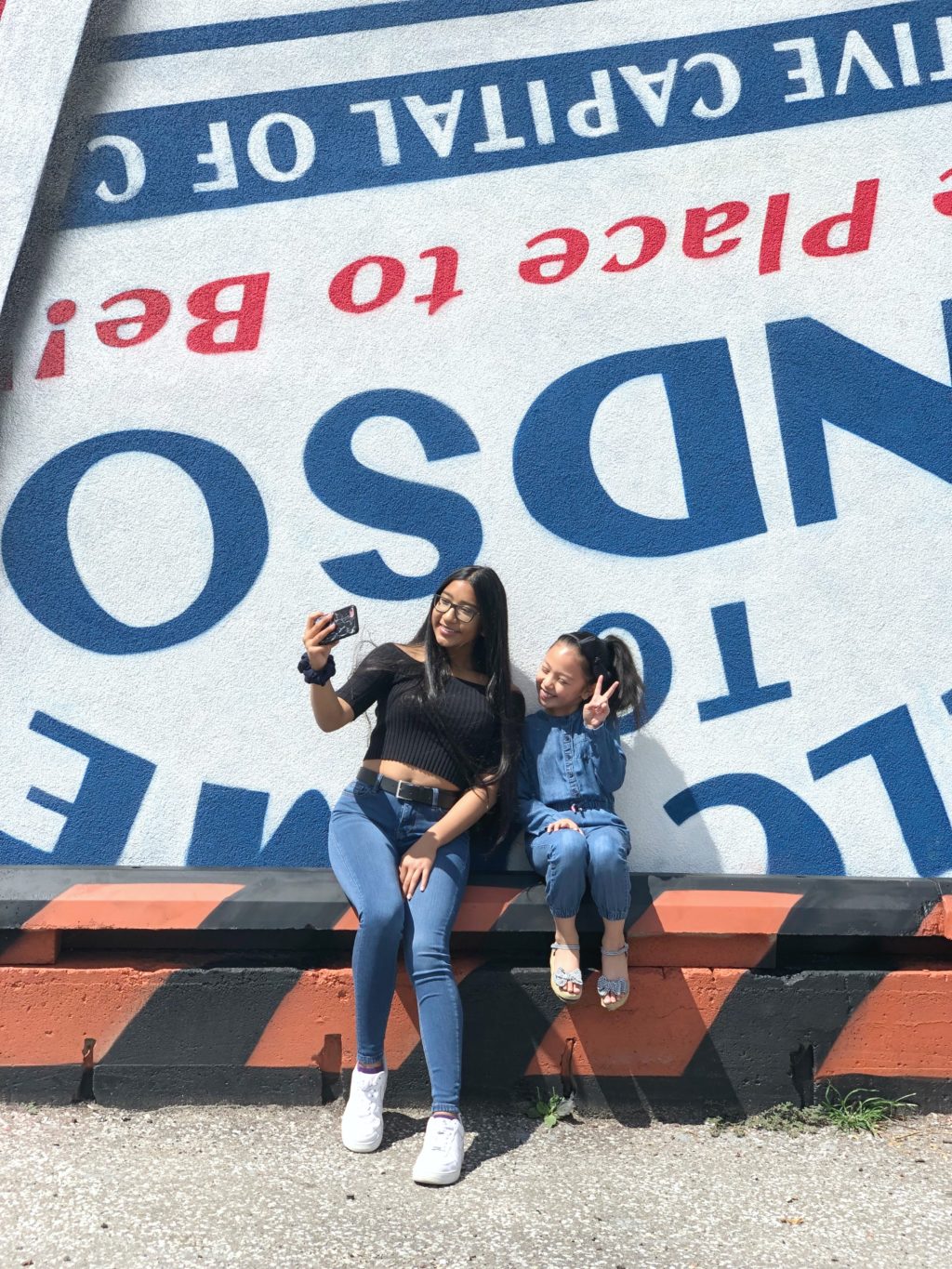 Two sisters, Gabby and Mimi, take a selfie in front of a murale in Downtown Windsor. See how TELUS can help keep families connected.