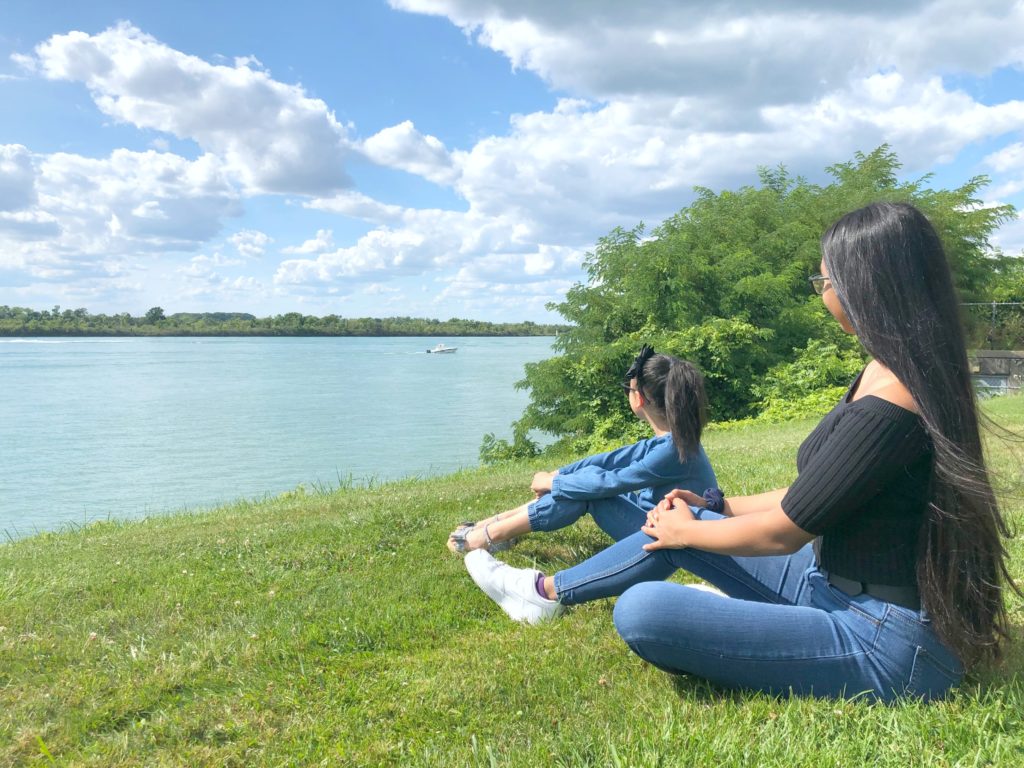 Gabby and Mimi sit on a hill side by the Detroit river, they're watching boats go by.