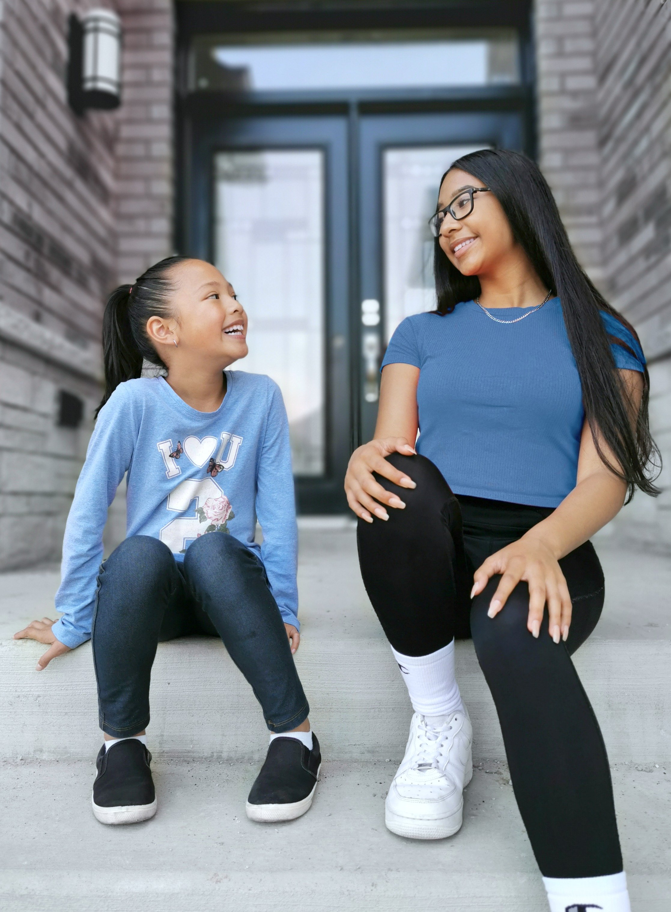 Mimi and Gabby sit on the doorstep smiling and laughing.