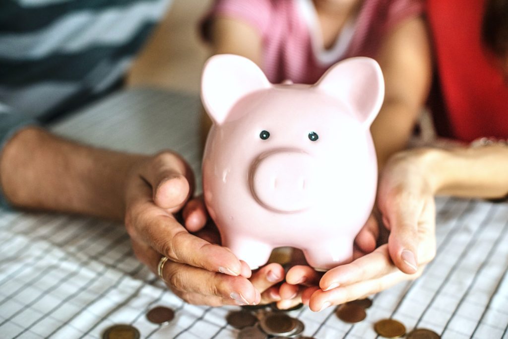 A couple and their daughter hold a piggy bank together. Coins surround the piggy bank. 