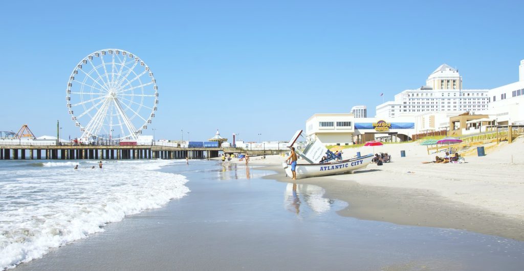 The beach with the pier in Atlantic City in the back. A person is shown with a boat that says, "Atlantic City."