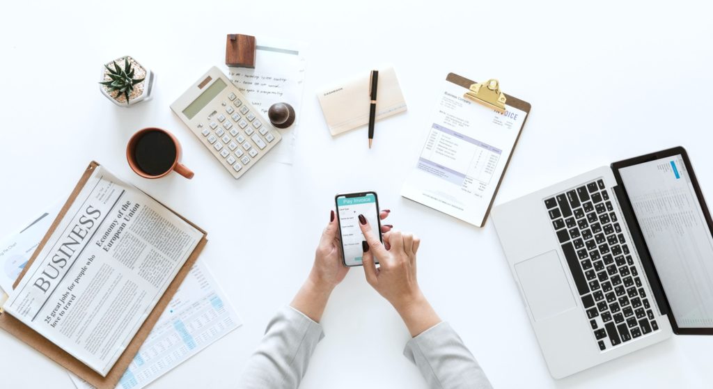 Woman surrounded by business necessities: laptop, coffee, invoices, paper, phone and more.