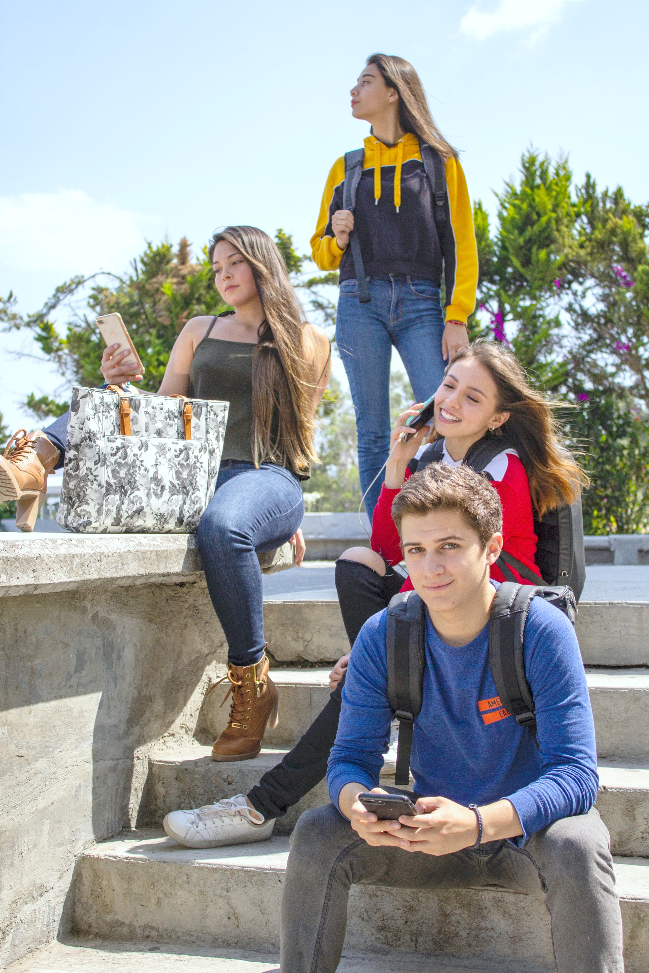 A group of teenagers sitting on a stairs on their phones and chilling on campus. 
