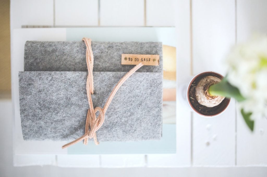 Grey agenda that says "to-do" list on a white wood table, a flower is seen from a bird's eye view. The agenda is to keep track of tasks that you really need to stop putting off.