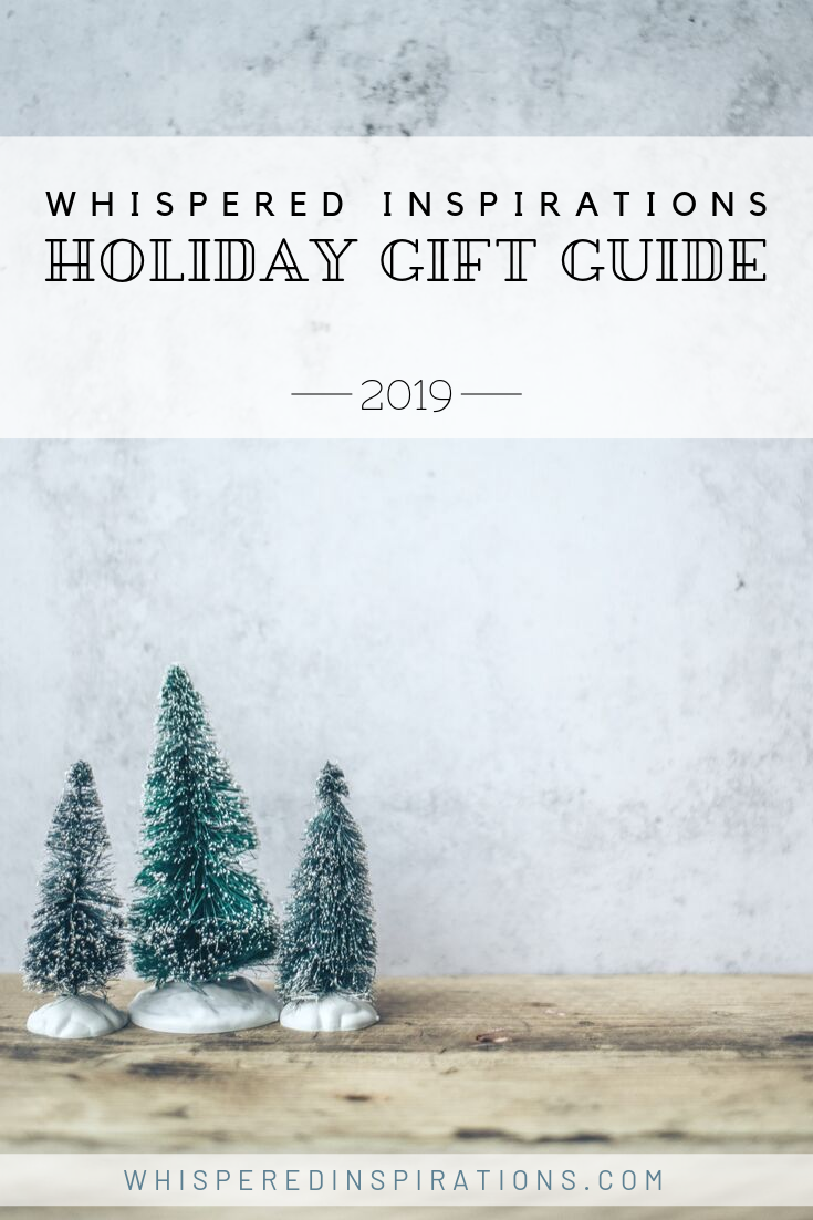 A stone background and a wooden table top. 3 little snow-covered pine tree figurines are on top of the table. A banner reads, "Whispered Inspirations, Holiday Gift Guide, 2019"