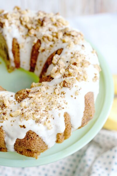 Glazed banana bread bundt cake on a green pedestal. It is glazed and topped with walnuts..