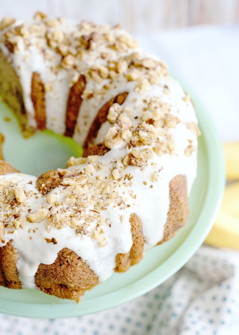 Glazed banana bread bundt cake on a green pedestal. It is glazed and topped with walnuts..