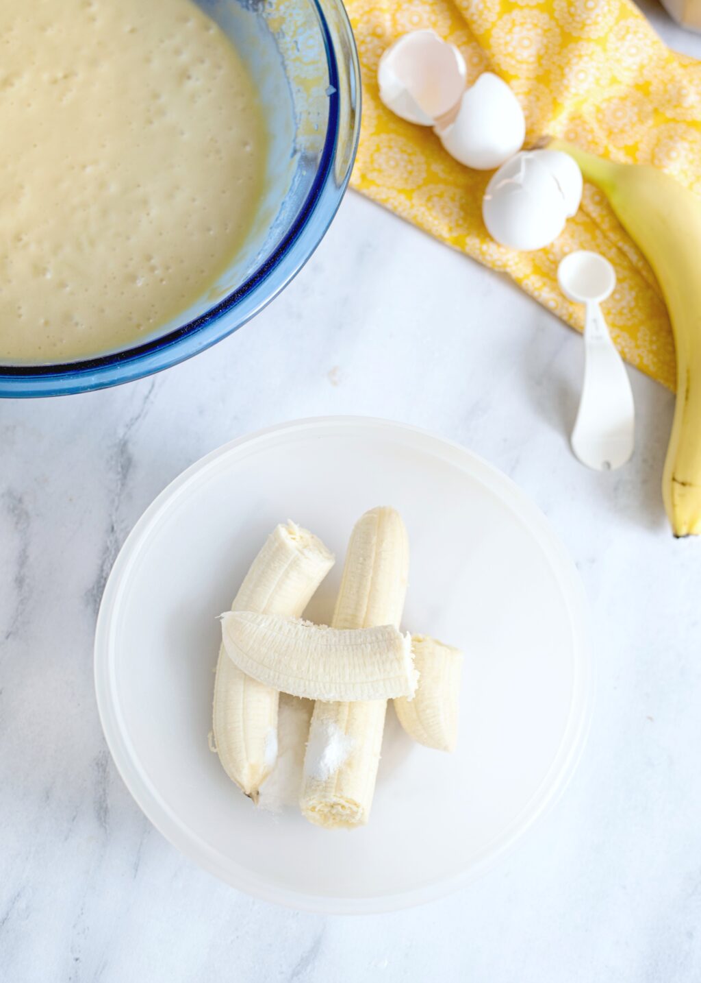 Chopped banana on a white plate, cake batter is in the background. 