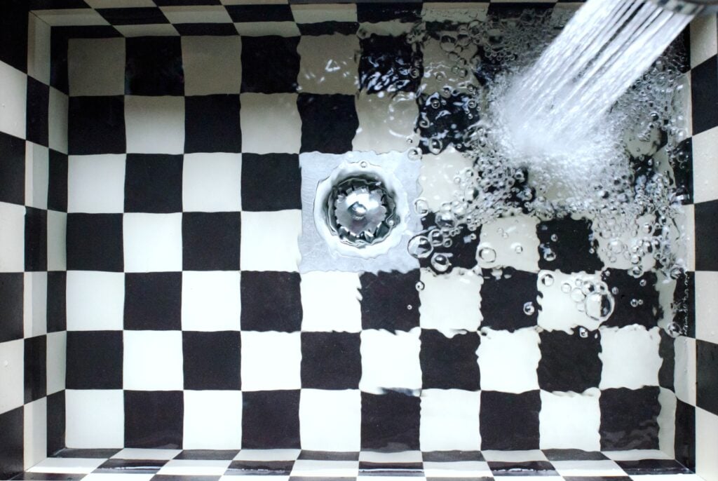 A checkered kitchen sink being filled up.