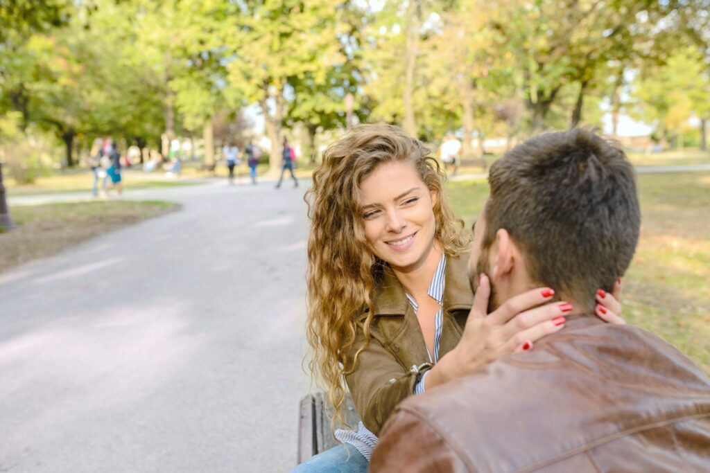 A couple sit on a bench, the woman caresses the man.