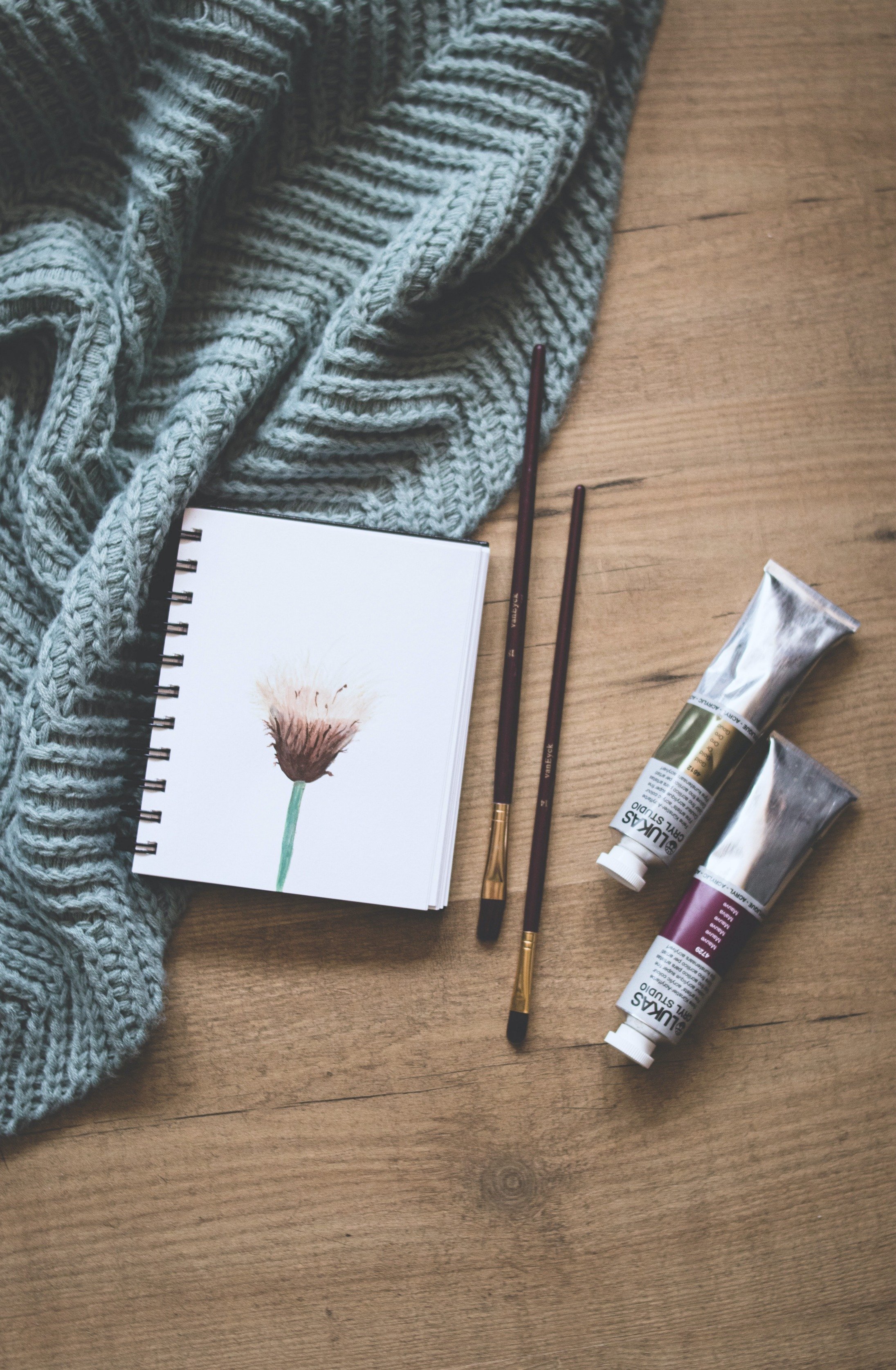 Throw blanket, notebook, and water colours on a wooden background.