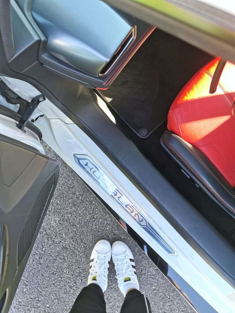 A view of Nancy's feet, she is wearing shell toe Adidas and getting into the Lambo. You can see the bottom part of the car and seat.