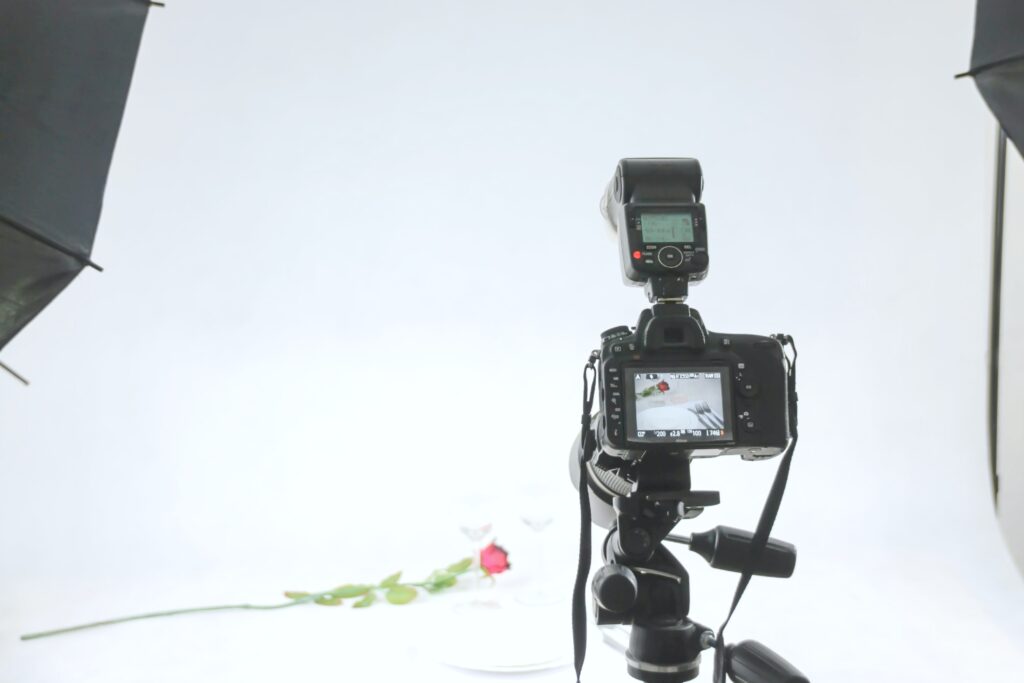 A camera on a tripod photographing two wine glasses and a rose. When hiring an artist or photographer, picking the right production house is so important.