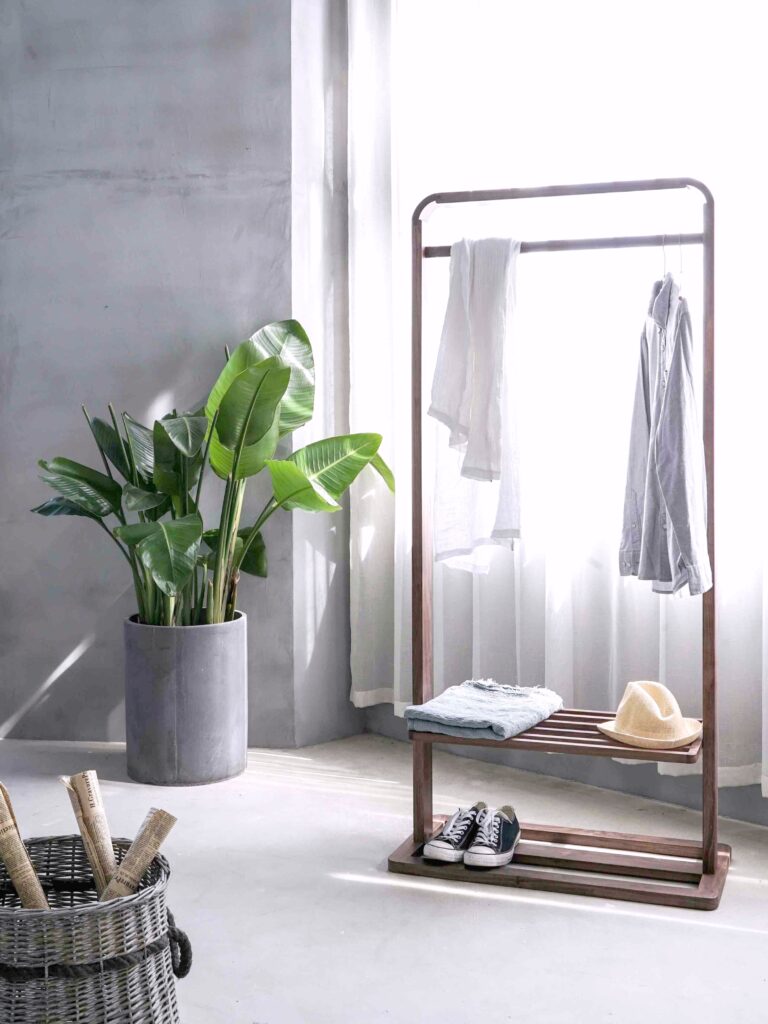 A gorgeous bedroom that has a wooden clothes rack and plants.