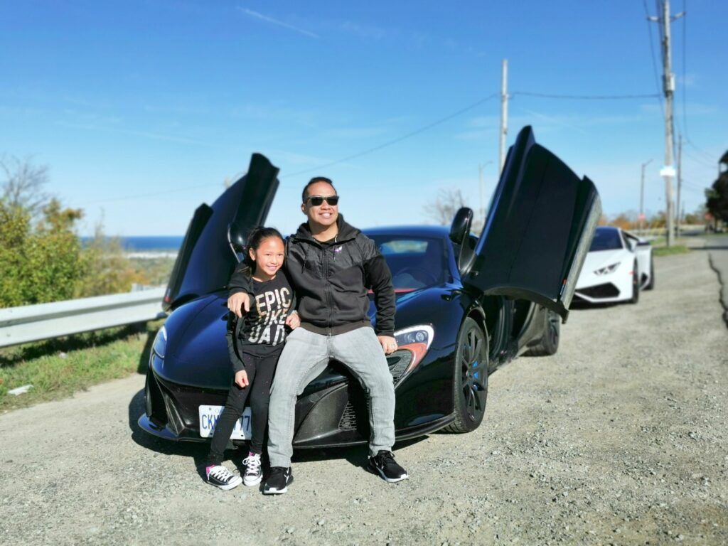 Mimi and Darasak sitting on the hood of a McLaren at a photo opp stop. 
