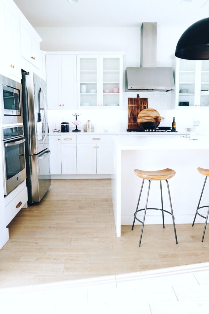 A white kitchen with black fixtures and natural wood stools. A suggestion for some kitchen design ideas for 2020.