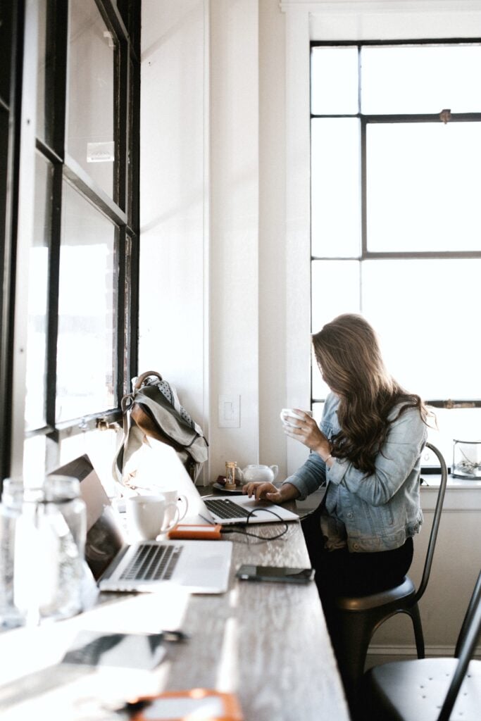 Woman sits in a cafe, sips on coffee, and uses her laptop.