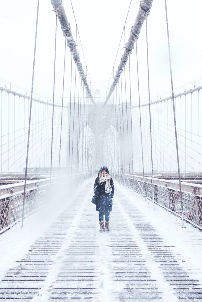 A girl stands and smiles on the NYC bridge. It's a cold, windy, winter wonderland.
