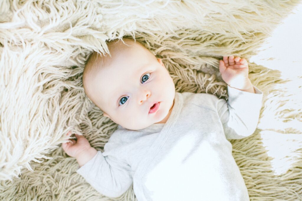 A baby laying on a blanket, he is looking at the camera. This baby could use one of the best baby pacifiers in 2020, like Chicco.