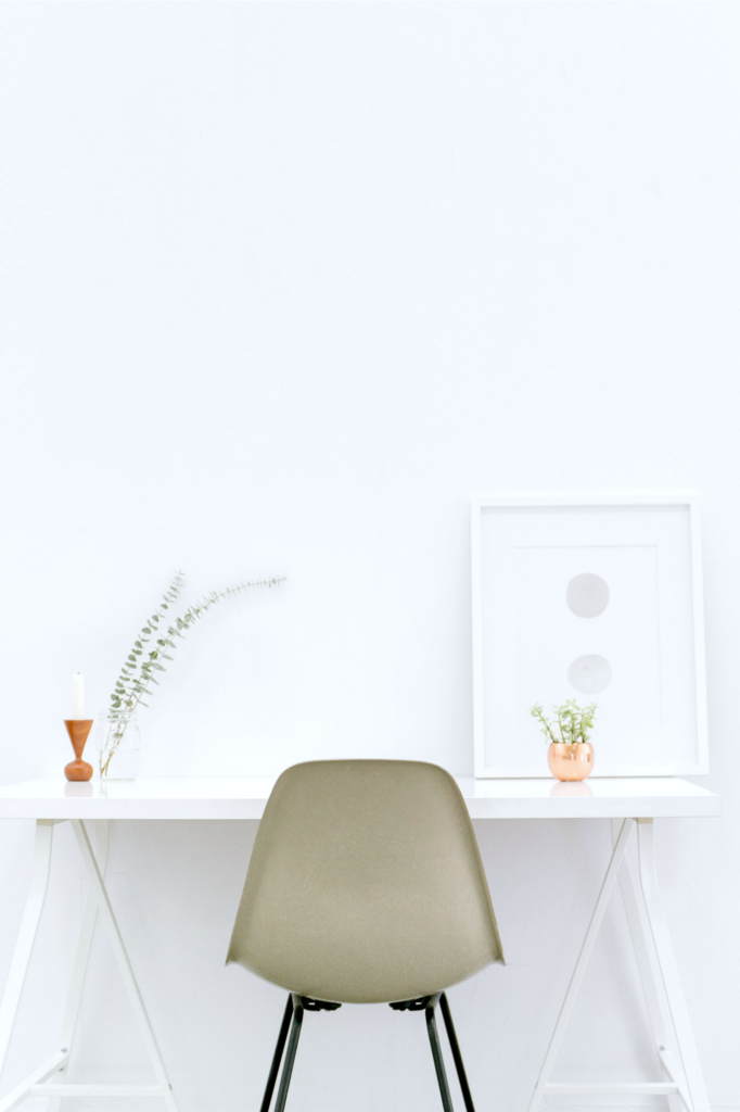 A white room with a white desk, a brown chair, and aluminium frame on top of desk.