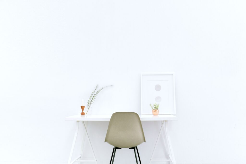 A white room with a white desk, a brown chair, and aluminium frame on top of desk. 