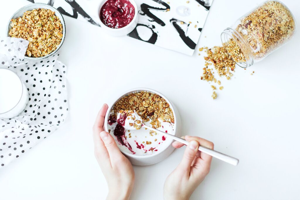 Woman eats yogurt parfait with granola and fruits, only her hands are shown and she is holding a spoon.