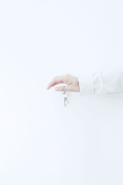 A person's arm and hand are against a white wall and holds a key.