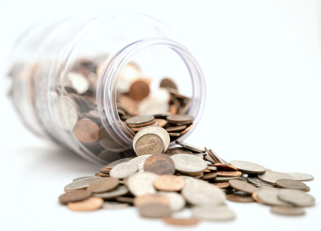 A jar is filled with coins and is on its side, while the coins spill out.