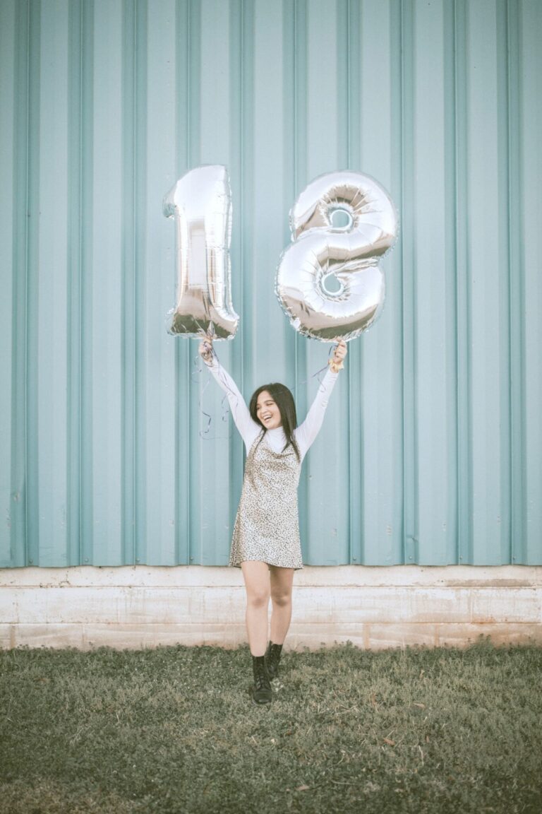 A teen girl holding up an 18 shaped balloon.