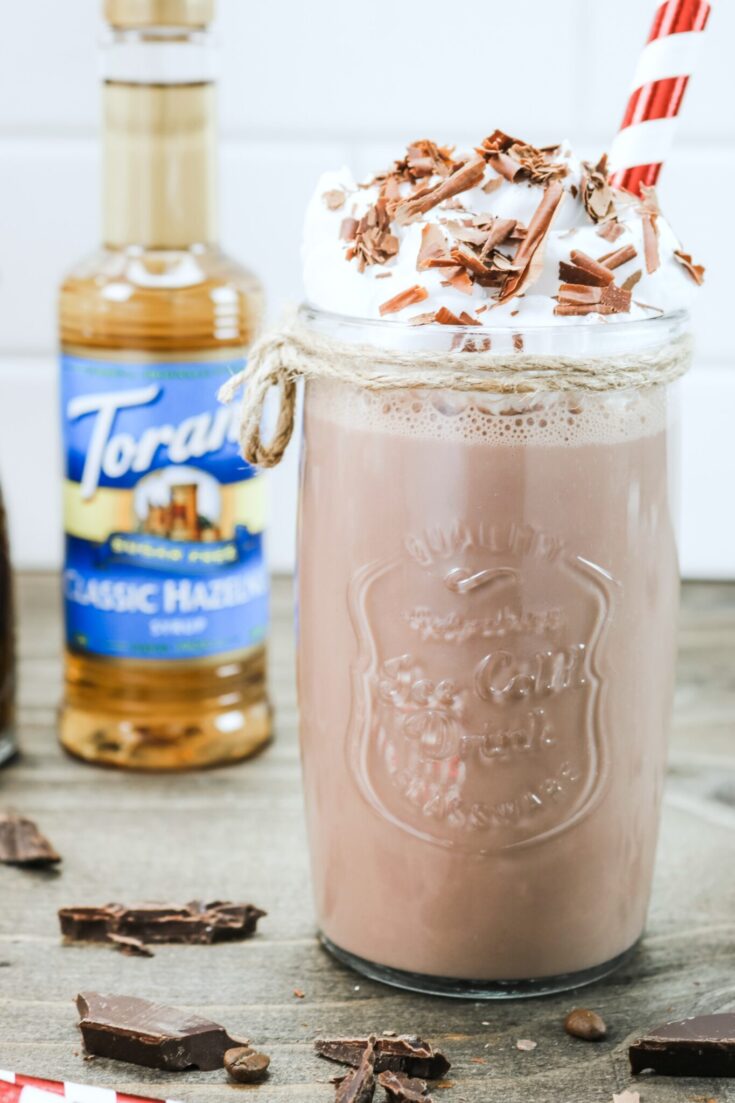 A close up of a Hazelnut Protein Iced Mocha made with Torani Sugar-Free Classic Hazelnut Syrup. A bottle is seen in the back.