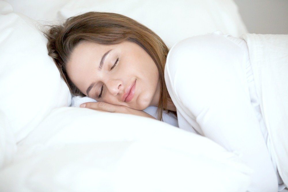 A woman sleeps peacefully on a white pillow and sheets. She uses hypnosis for sleep and sleeps soundly.