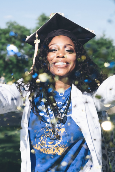 Woman is graduating after forging a career path in healthcare. She is wearing a graduation cap and a stethoscope and throwing glitter in the air.