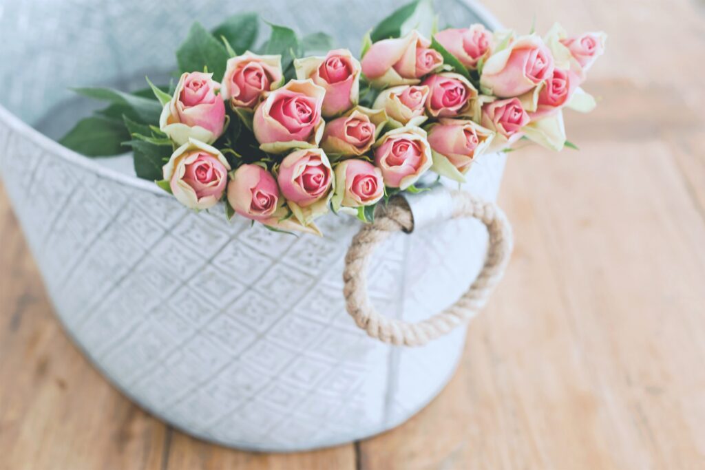 A bin with pink roses on a wooden table. 