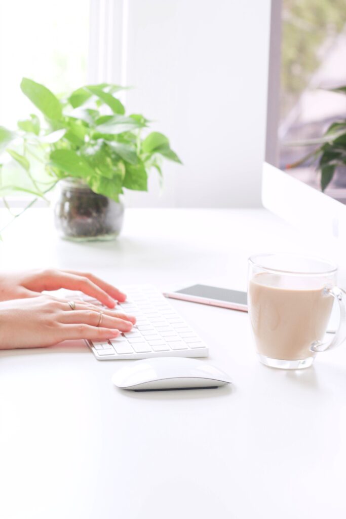 Woman's hand typing on a keyboard and mouse, with a cup of coffee. 