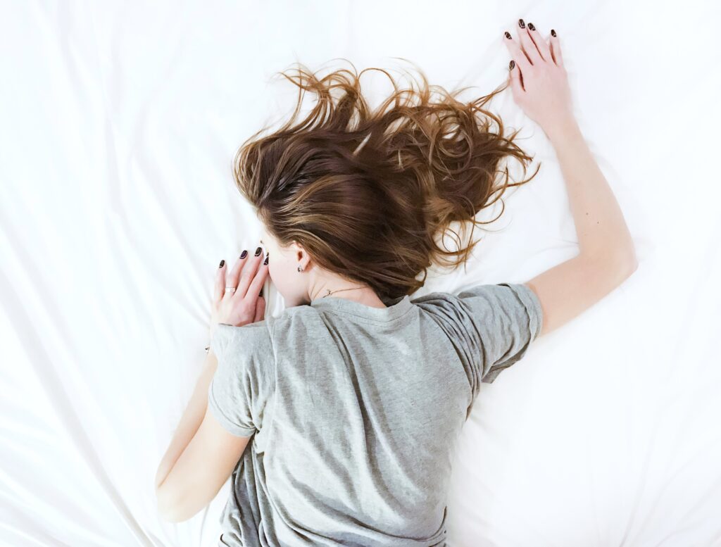 Woman lies on her stomach, tired, in bed on a white sheet.