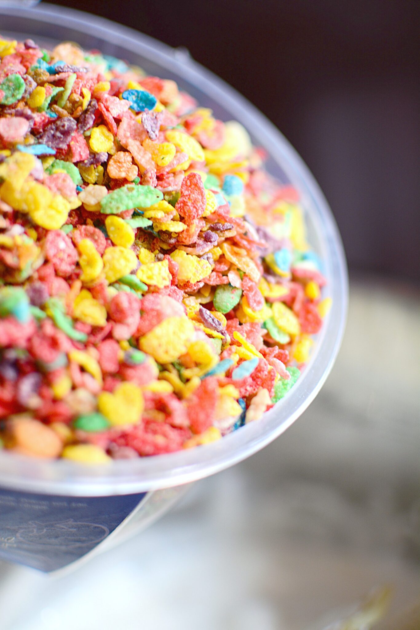 A close up of a cup of Fruity Pebbles cereal being poured into marshmallow mix. 