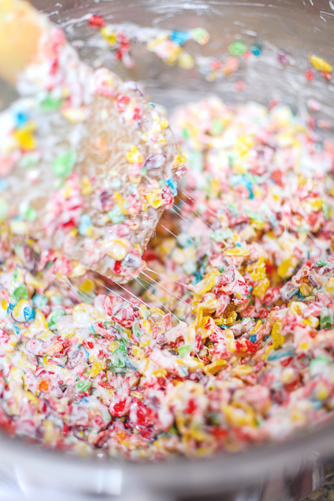 The Fruity Pebbles cereal being mixed into the marshmallow mix. 