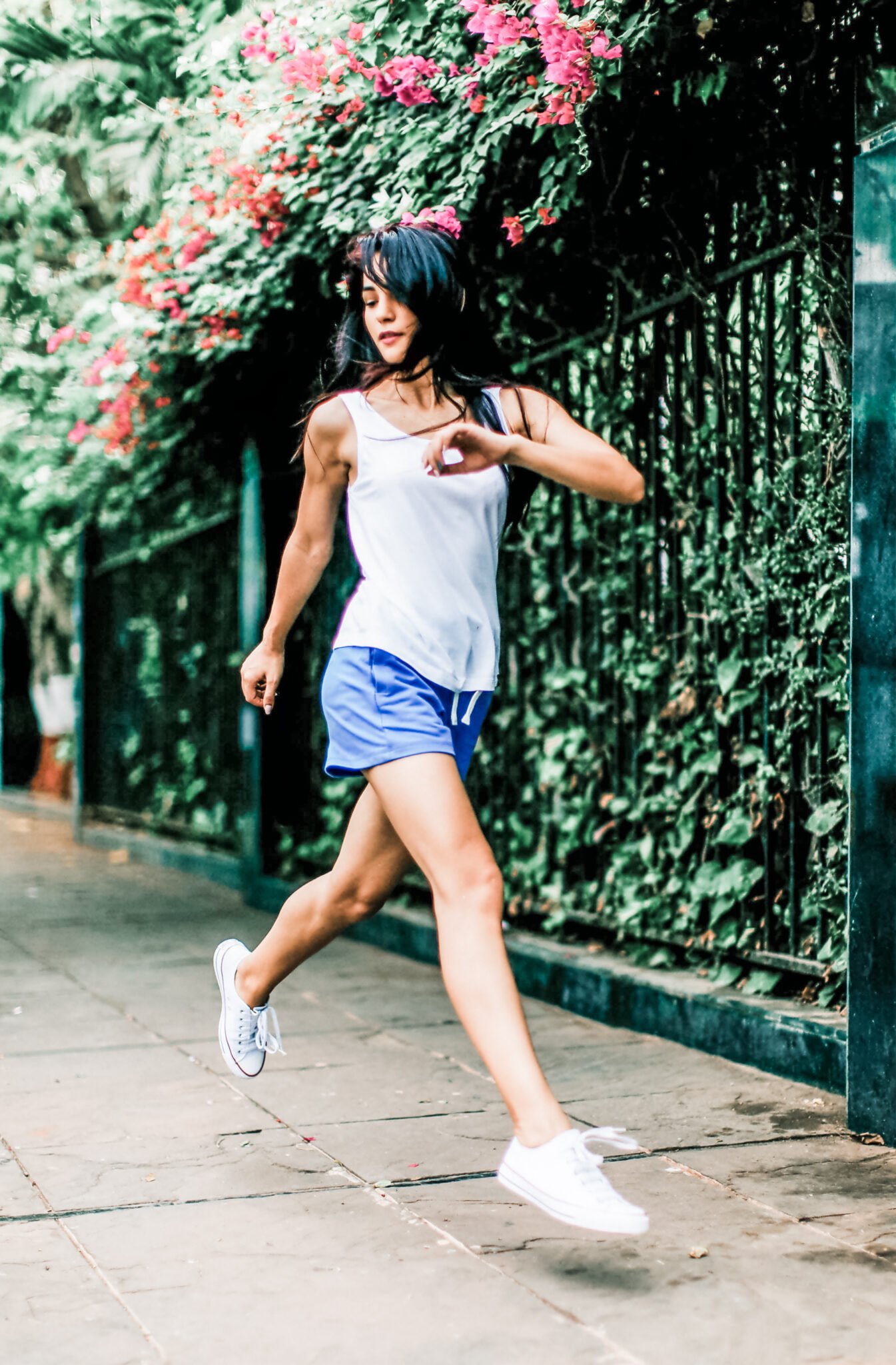 Strong woman running down the street, flowers are behind her, she is midair.