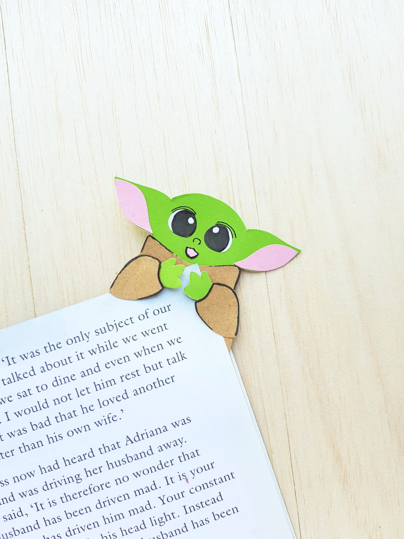 Baby Yoda holding the corner of book, a paper craft used as a bookmark. 