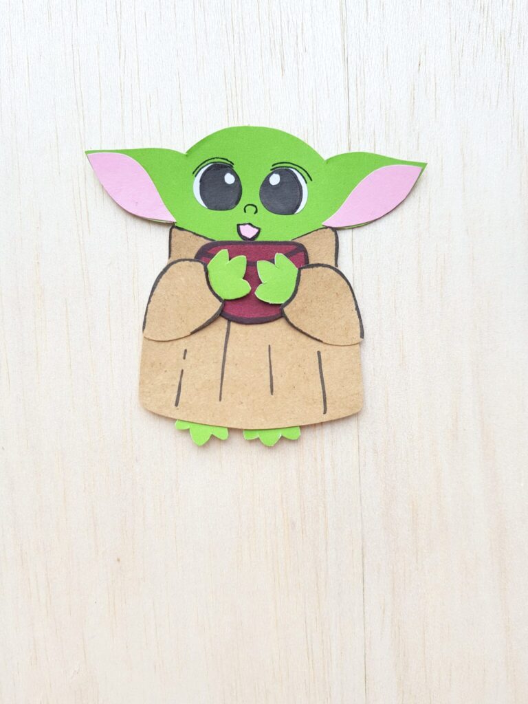 Baby Yoda holding the corner of book, a paper craft used as a bookmark.