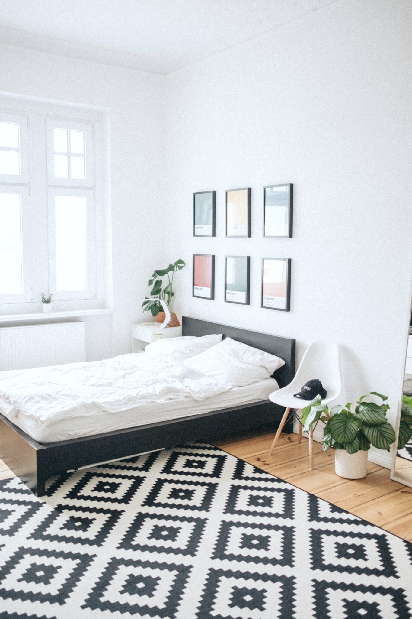 A bedroom with a black and white rug, clean, minimal style, with plants. 