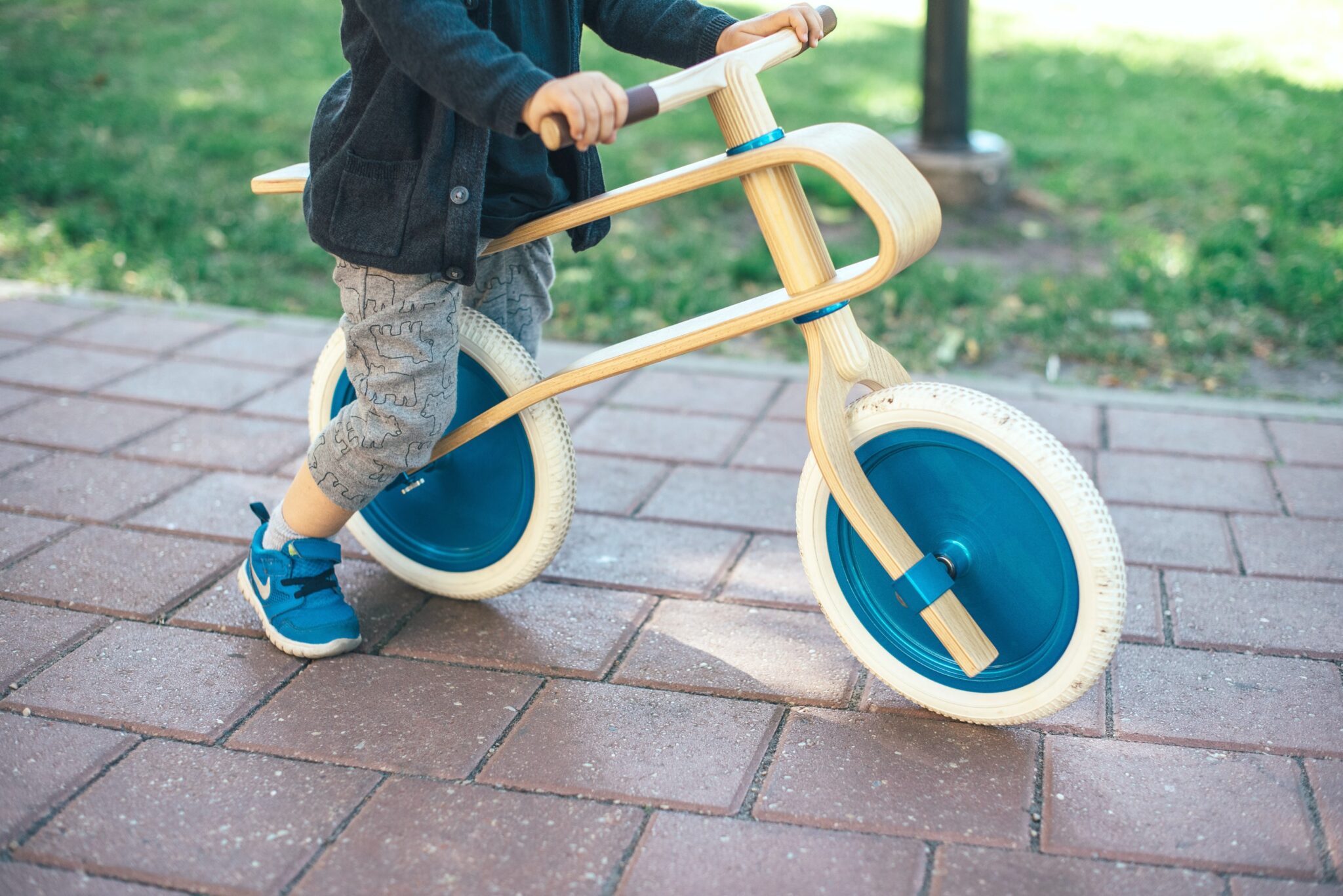 A close up of a little boy with blue Nike shoes, sitting on a wood and blue balance bike.