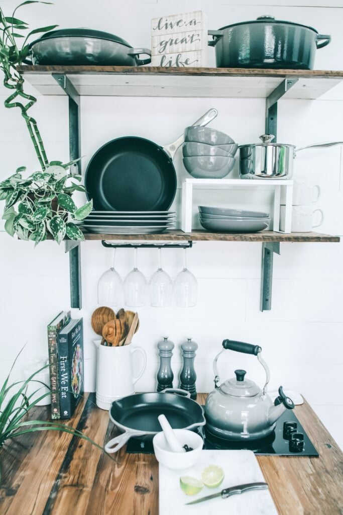 A gorgeous kitchen with butcher block wood counters, shelves, and cookware being displayed. Showing what is the healthiest cookware to use.