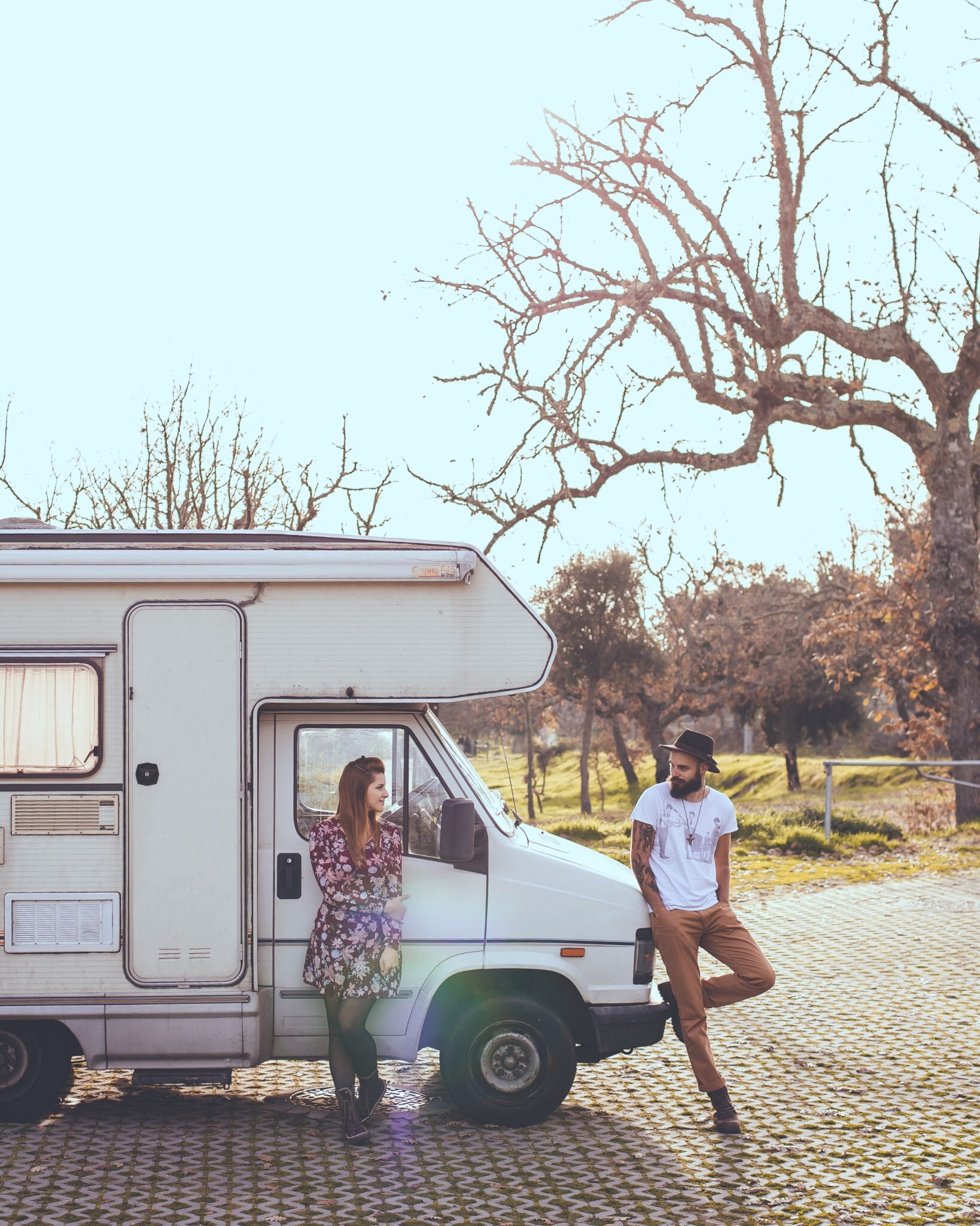 A young, hip, couple lean against their vintage motorhome.