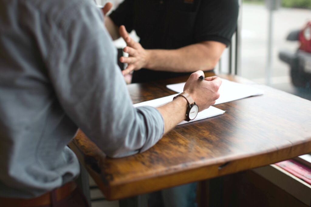 Two people argue over paperwork, their faces are not seen only their hands and the paper work on the table.