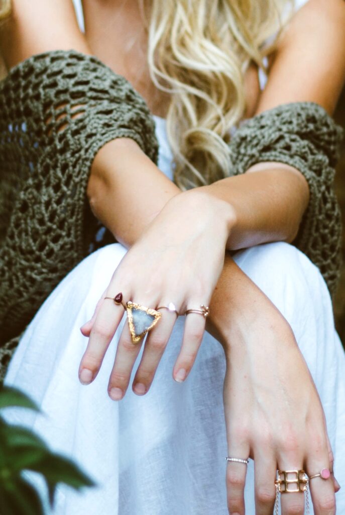 A close up of a woman's arms and skirt, her statement rings are the focus. She has the tips of her blond hair showing. 